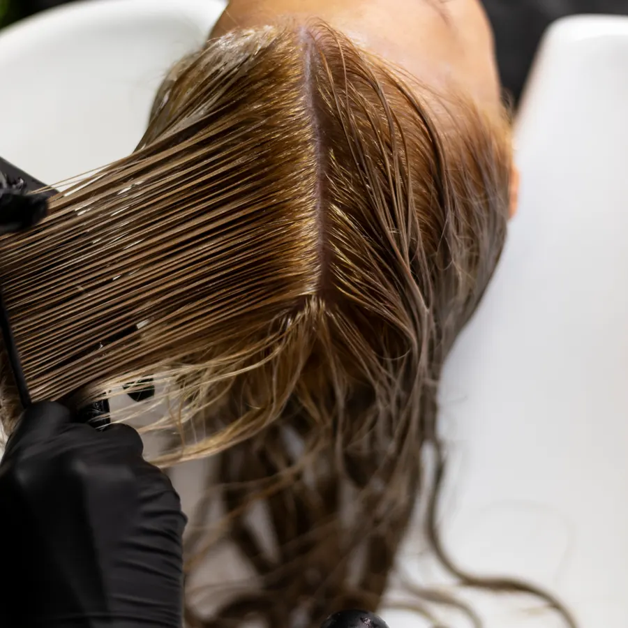 Lavaggio al lavatesta: le mani coi guanti neri sciacquano i capelli castani